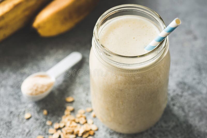 Protein Milkshake With Oats, Banana in jar with paper drinking straw on concrete background. Closeup view, selective focus. Concept of vegan sporty healthy lifestyle. Protein Milkshake With Oats, Banana in jar with paper drinking straw on concrete background. Closeup view, selective focus. Concept of vegan sporty healthy lifestyle